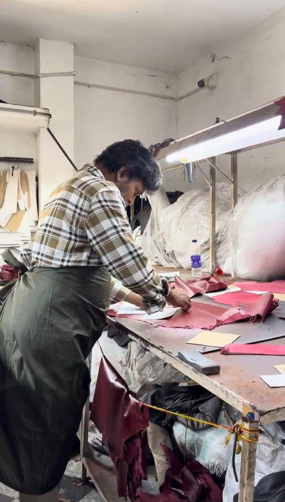 A CLF craftsman hand-cutting burgundy leather panels on the workshop table